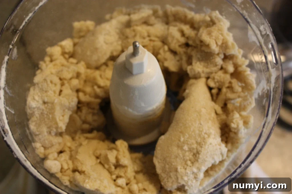 Smooth, pale yellow cardamom pistachio cookie dough collected in the bowl of a food processor after pulsing.