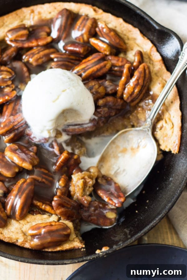 A large spoonful of warm skillet blondie with bourbon caramel pecans being scooped out, showing its gooey texture.