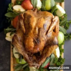 Overhead view of Herb Roasted Turkey on a cutting board garnished with apples and herbs.