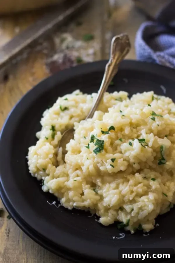 Easy Parmesan Risotto 3 A black plate with easy risotto topped with fresh chopped parsley and a fork, ready to be enjoyed
