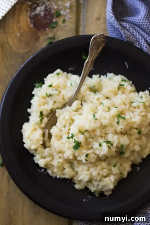 Easy Parmesan Risotto 4 Overhead view of creamy parmesan risotto garnished with fresh chopped parsley on a black plate with a fork, ready to eat