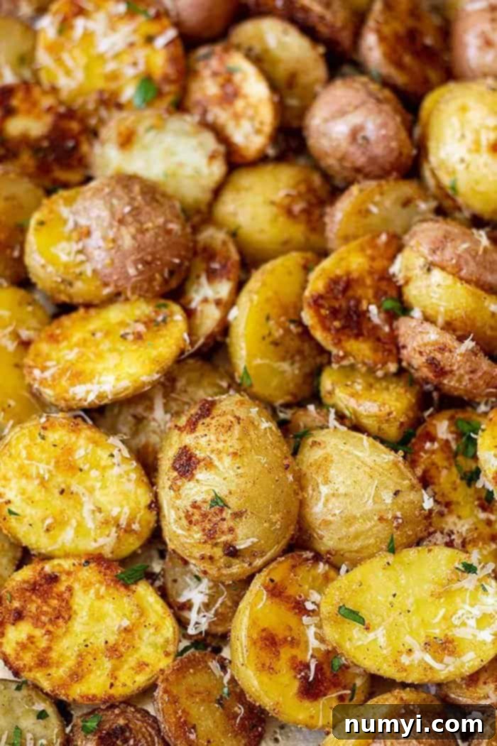 Garlic Parmesan Roasted Potatoes 3 Close-up of golden roasted Parmesan potatoes, glistening with olive oil and sprinkled with fresh Parmesan and green parsley.
