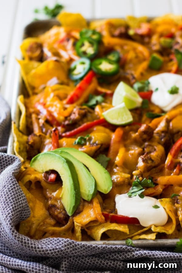 A large sheet pan of loaded chicken fajita nachos, perfect for game day or a family meal, generously topped with melted cheese, seasoned chicken, and colorful bell peppers.