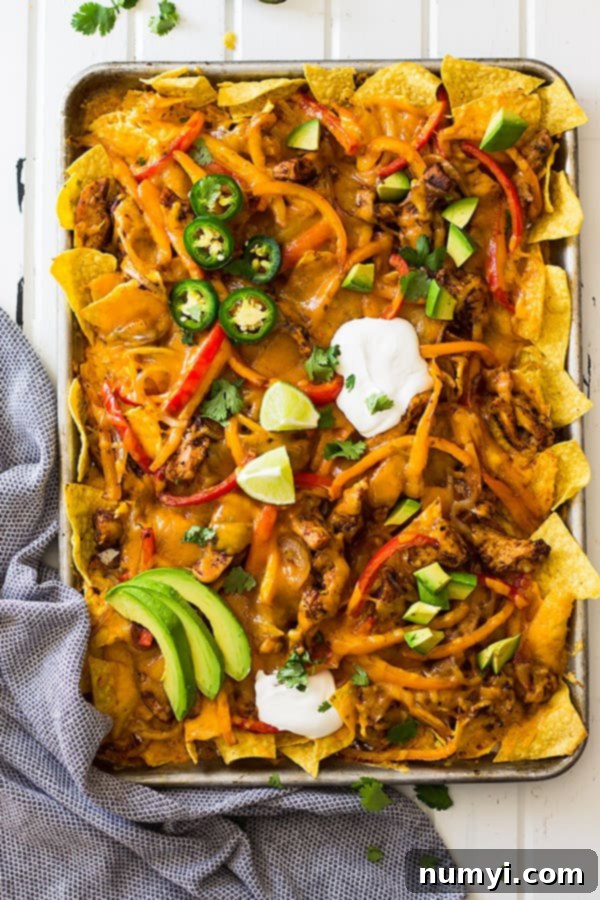 Close-up of chicken fajita nachos on a sheet pan, showing layers of crispy tortilla chips, sautéed chicken, and tender-crisp fajita vegetables before the final cheese layer.