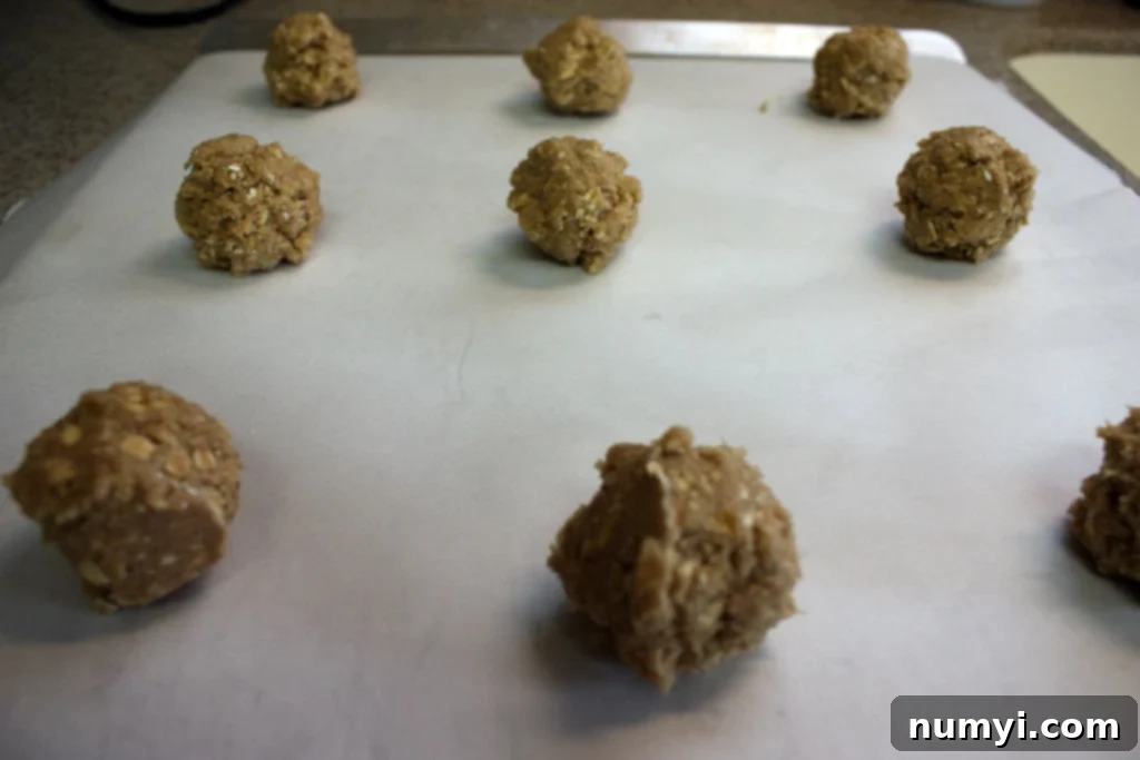 Oatmeal cookie dough balls on a parchment paper lined baking sheet.