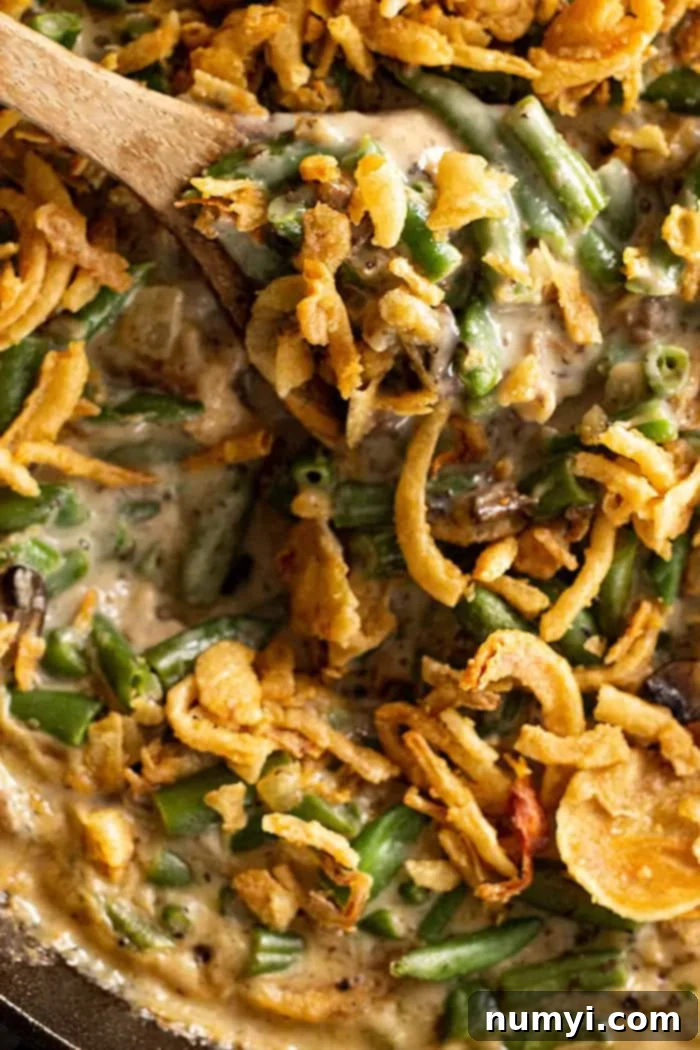 Wooden spoon stirring homemade green bean casserole with fried onion topping. 
