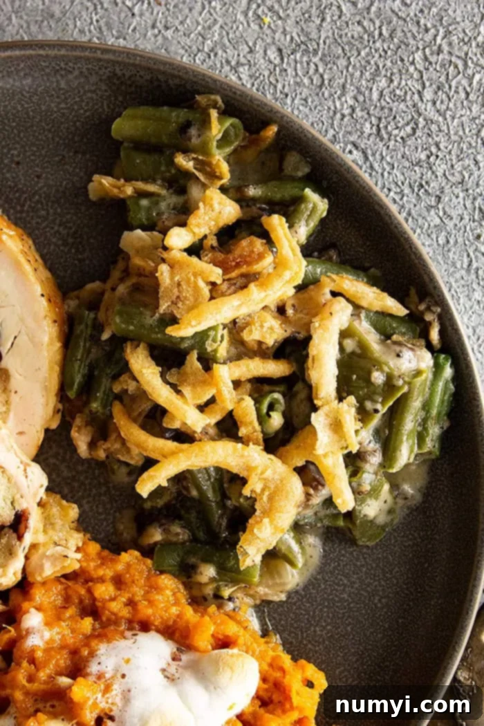 Serving of green bean casserole on gray plate with turkey and sweet potatoes. 