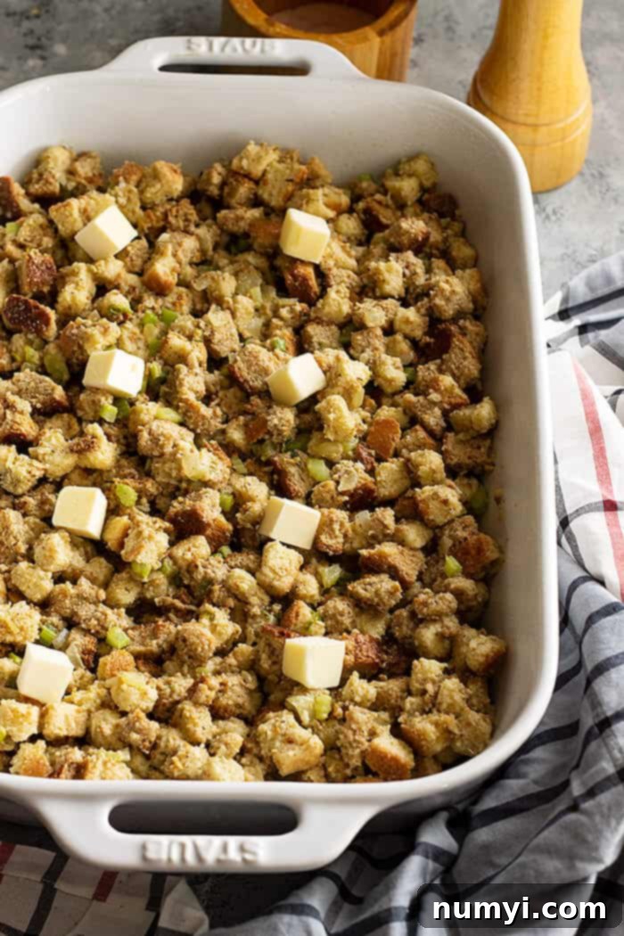 herb stuffing in a baking dish dotted with butter ready to be baked