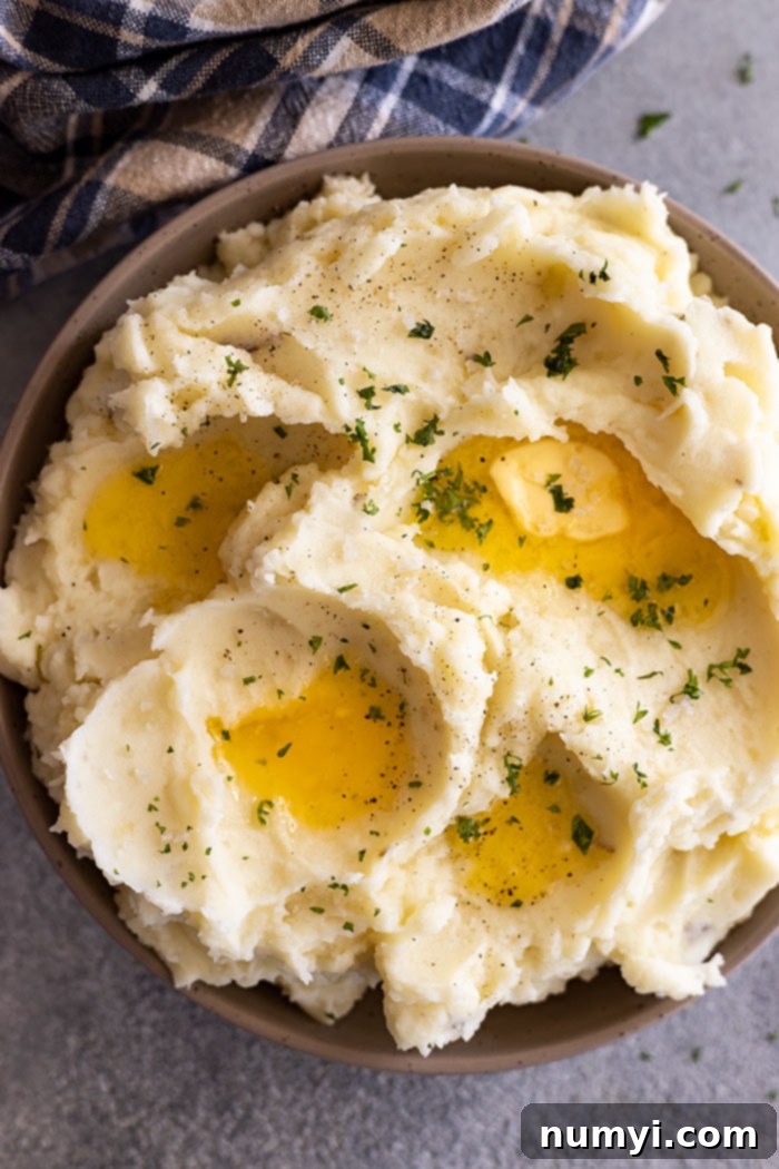 Effortlessly Delicious Garlic Mash 5 A bowl of creamy garlic mashed potatoes topped with fresh parsley, next to a whisk and a small pot.