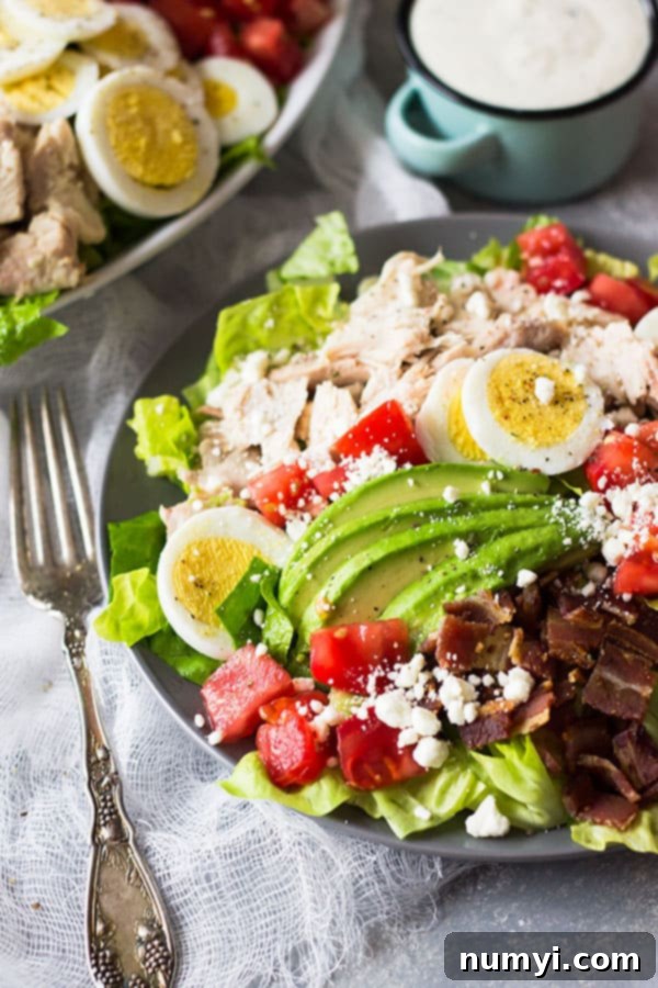 A perfectly arranged Turkey Cobb Salad on a light wooden background, featuring distinct rows of colorful ingredients: crisp romaine, tender turkey, crumbled bacon, bright red tomatoes, creamy avocado, chopped hard-boiled eggs, green onions, and feta cheese.
