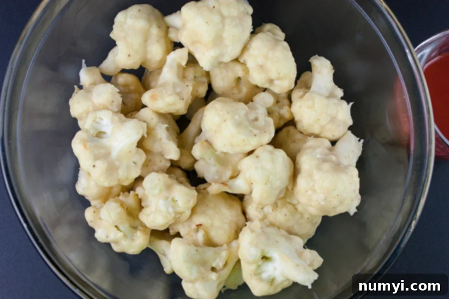 Golden brown, crispy baked cauliflower bites served in a clear glass bowl, showcasing their texture before being tossed in the signature buffalo sauce.