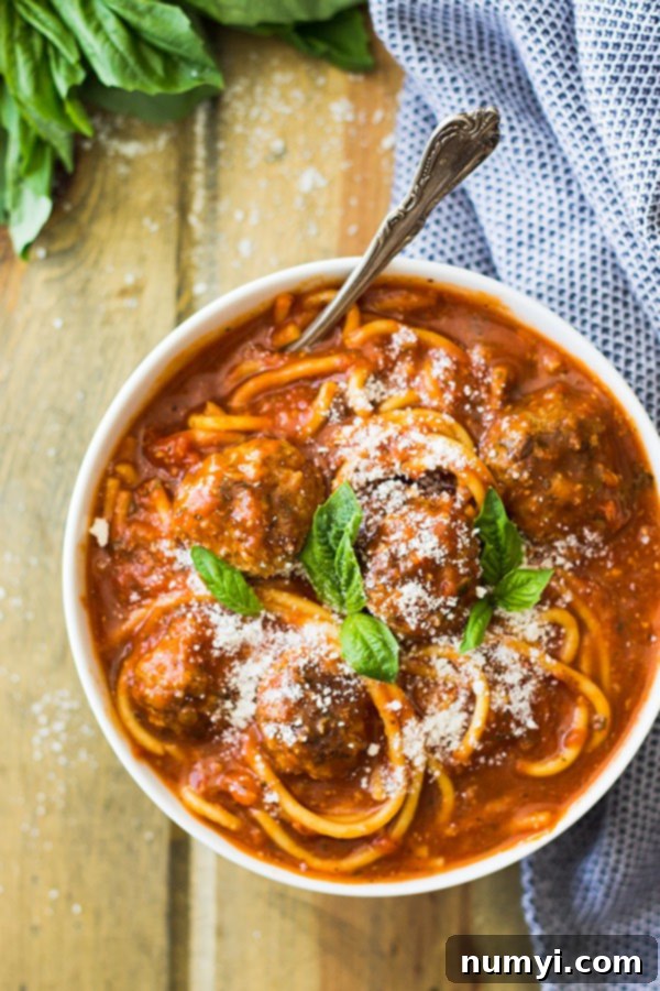 A bowl of Slow Cooker Spaghetti Meatball Soup with fresh Parmesan and basil