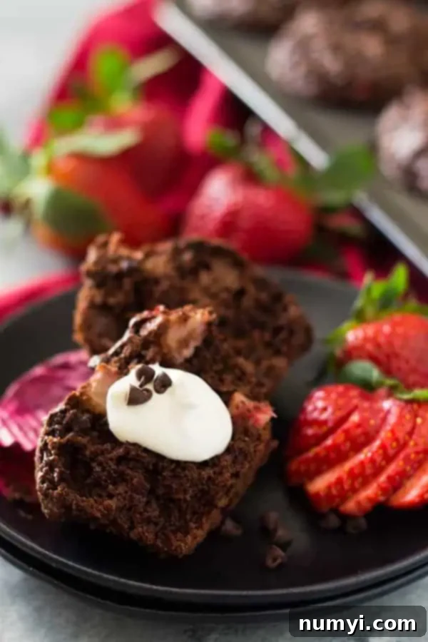 a chocolate strawberry muffin cut in half with a dollop of whipped cream and extra chocolate chips on top, ready to be served