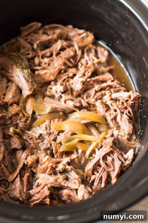 Shredded, fall-apart tender beef and thinly sliced onions simmering in a crockpot, surrounded by a rich, savory au jus.
