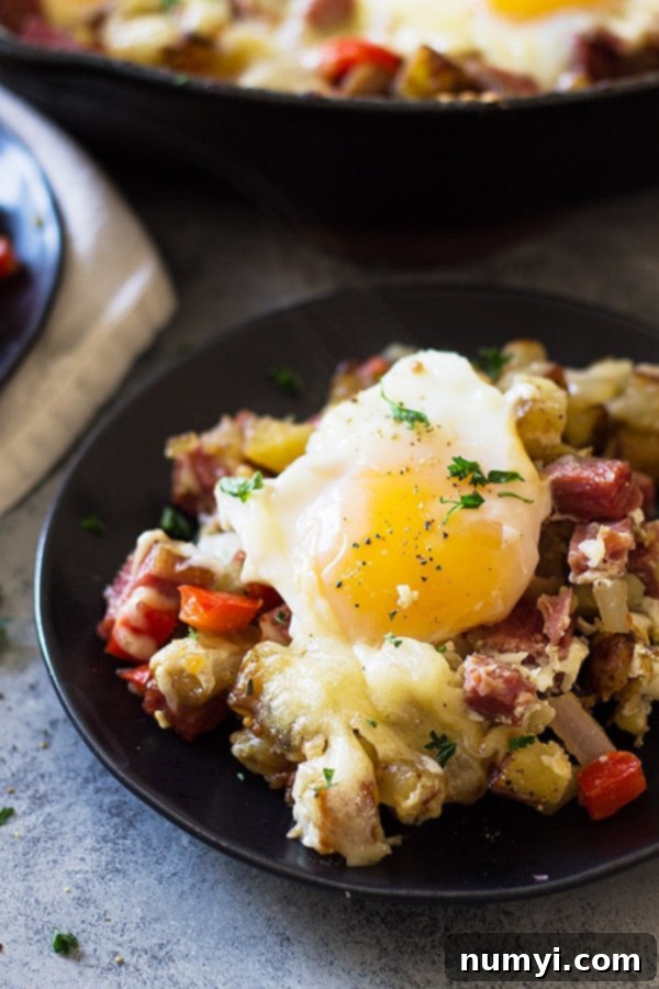 A pan of sizzling Cheesy Corned Beef Hash, showcasing crispy potatoes, diced corned beef, and colorful vegetables before eggs are added