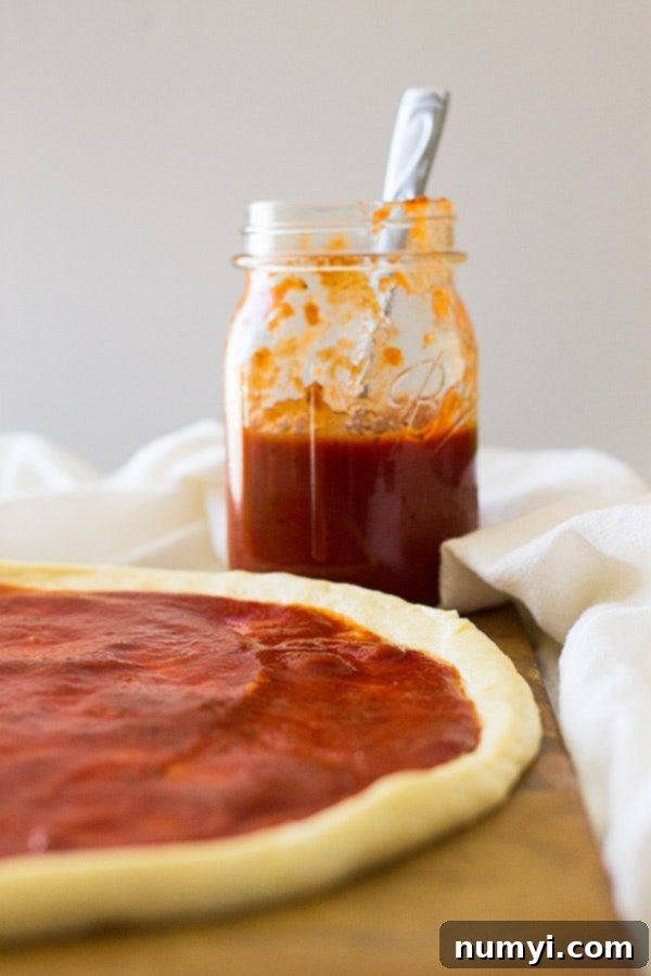 Close-up of a spoon stirring homemade pizza sauce in a saucepan on the stove, showing its smooth, rich texture and inviting aroma.