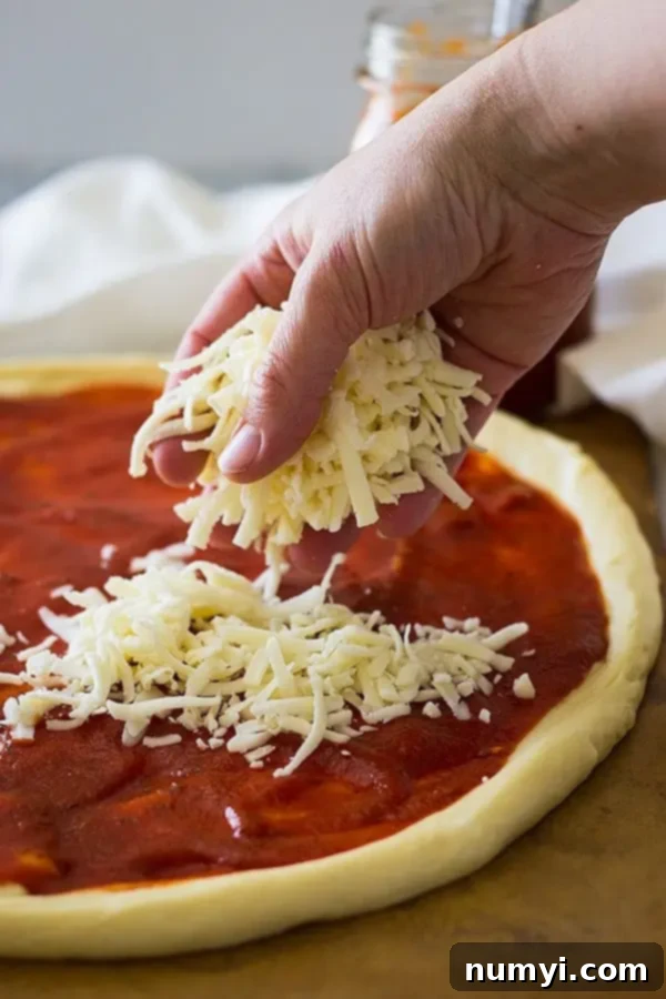 Perfectly Homemade Cheese Pizza 5 closeup: sprinkling pizza with cheese