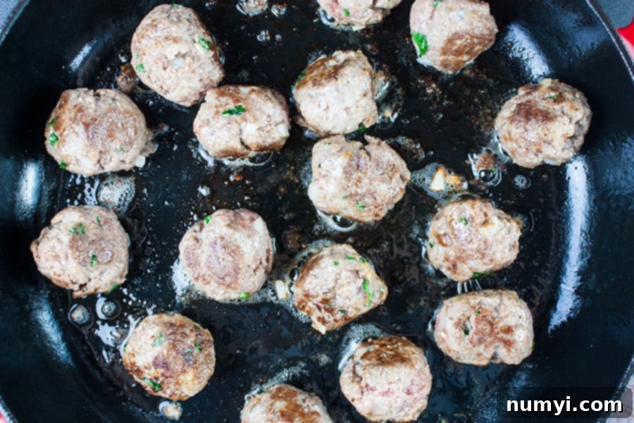 Swedish meatballs browning in a cast iron skillet, showcasing their delicious crust.