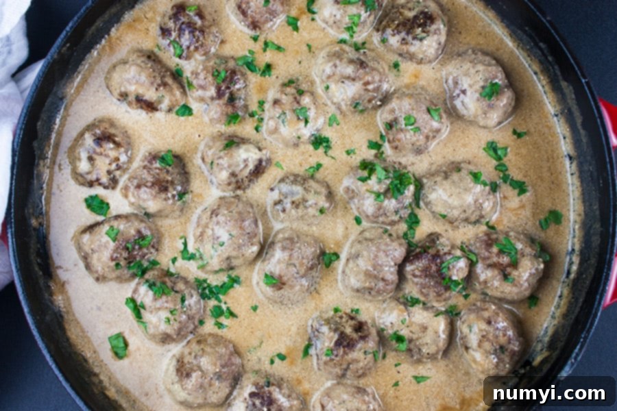 Swedish meatballs simmering in the creamy sauce in a cast iron skillet.
