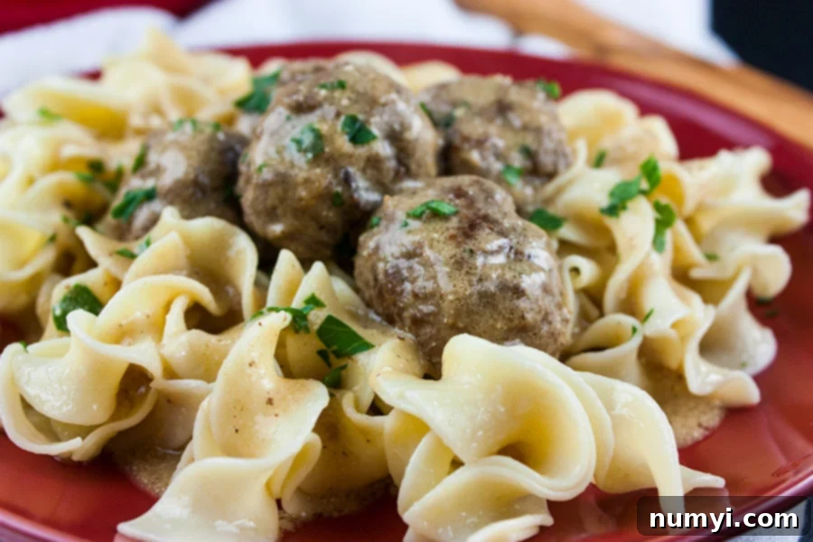 Plated Swedish Meatballs over egg noodles on a red plate, garnished with parsley.