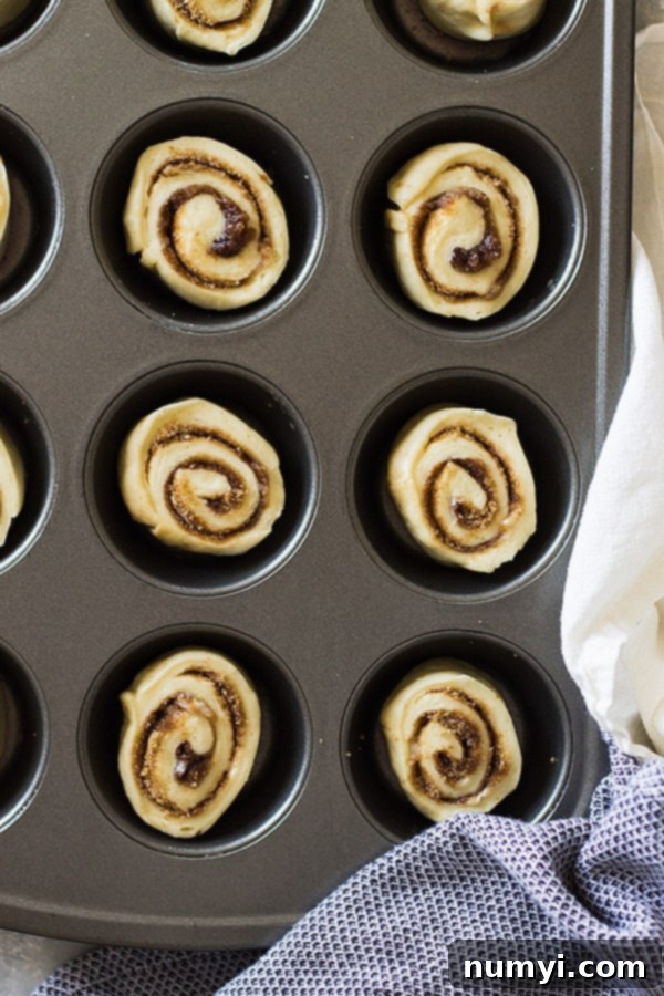 Fluffy homemade cinnamon roll muffins baked in a muffin tin, topped with a sweet vanilla icing, perfect for a delightful breakfast or brunch.