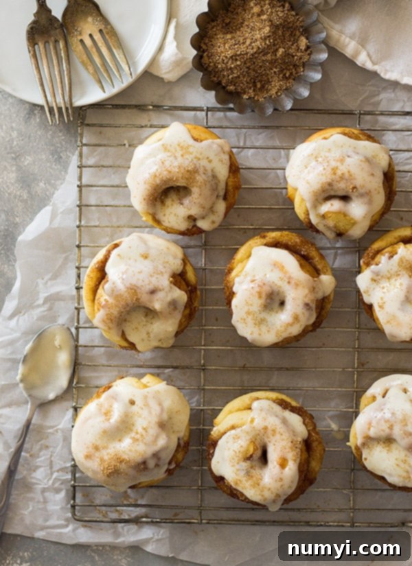 Four freshly baked cinnamon roll muffins on a wire rack, waiting for their delicious vanilla icing.