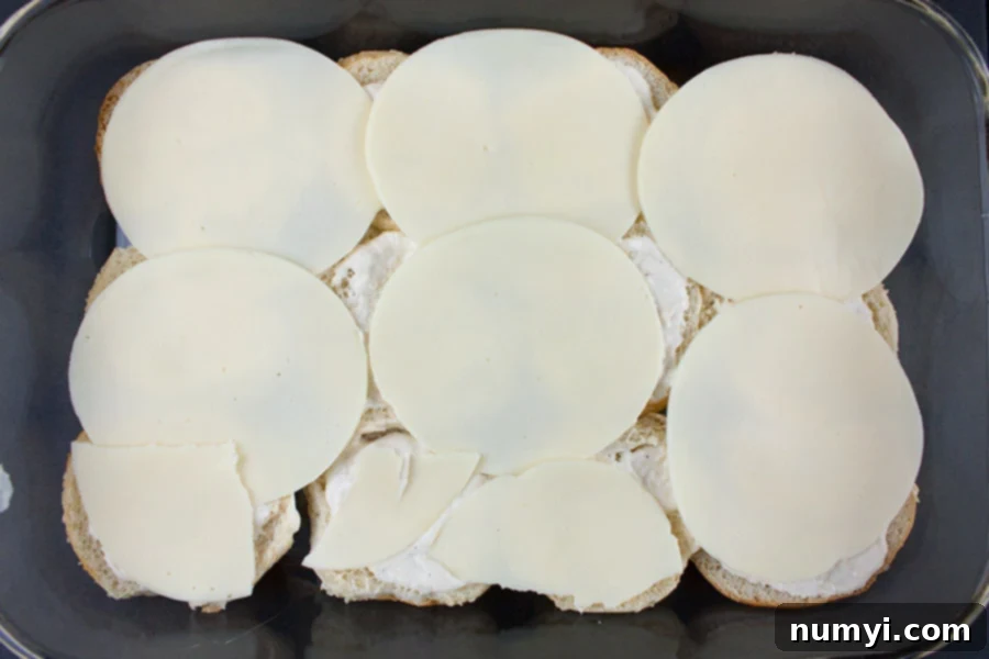 Smoky Roast Beef Sliders with Zingy Horseradish 5 Cheese slices layered over the prepared bottom buns in a baking dish.