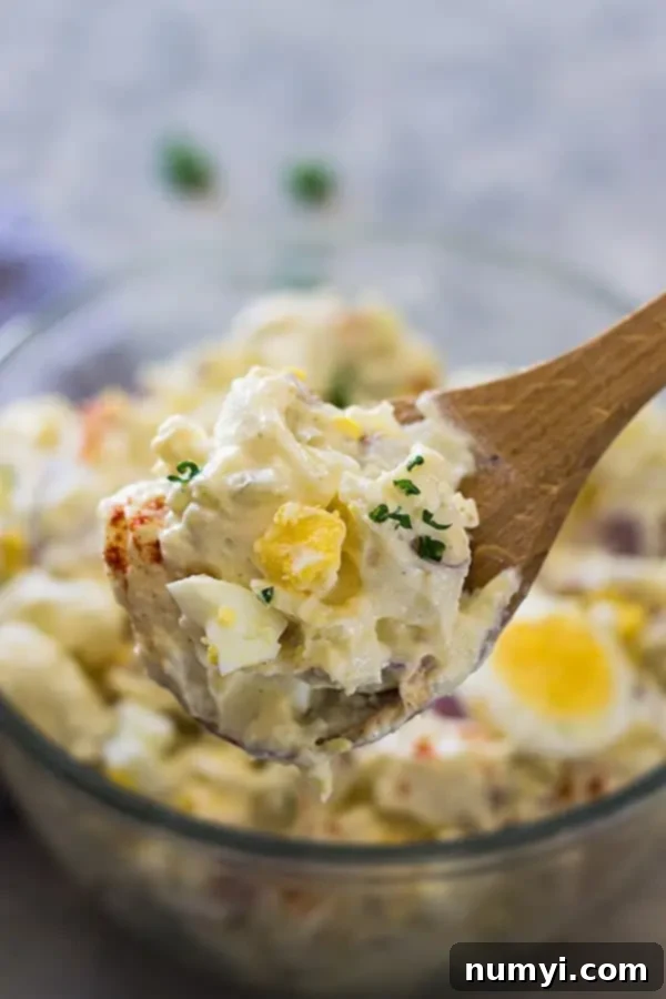 Grandma's Potato Salad 4 A close-up of a serving of creamy potato salad on a wooden spoon, garnished with fresh parsley.