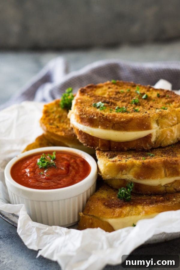Gourmet Italian Grilled Cheese 2 Two golden-brown Italian grilled cheese sandwiches, perfectly sliced to reveal gooey Provolone, served next to a small white bowl of rich pizza sauce for dipping.