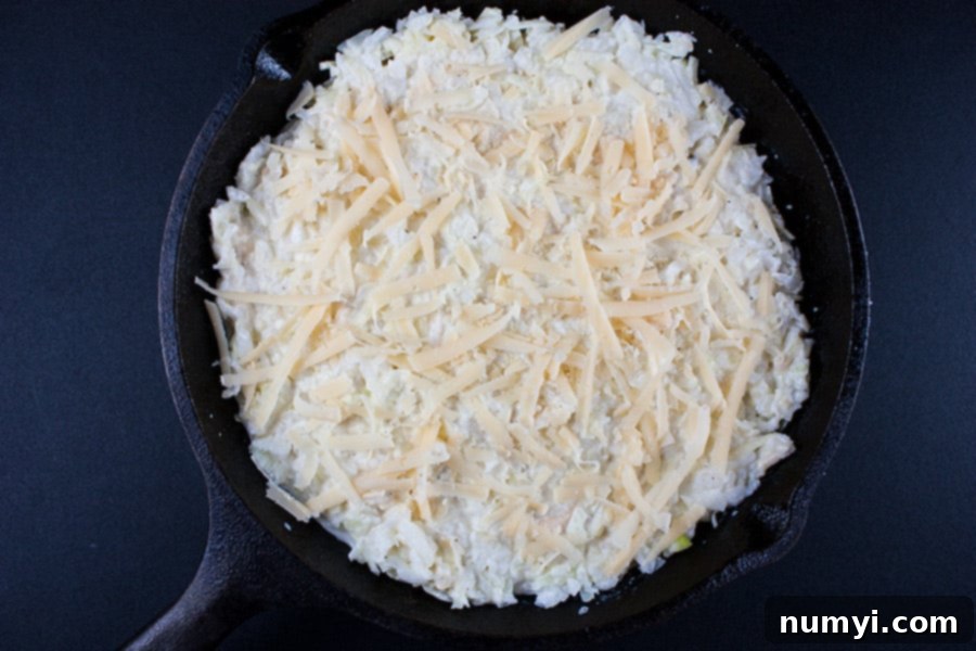 Baked Vidalia Onion Dip in a cast iron skillet topped with shredded cheese before baking.