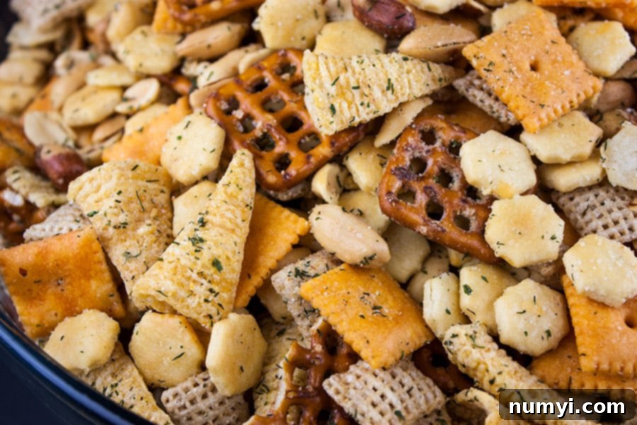 A glass bowl filled with freshly baked Ranch Party Mix, featuring a mix of golden crackers and nuts, ready to be served at a party.