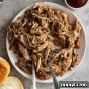 Overhead view of pulled pork on a white plate with two forks in the meat. Buns and bbq sauce off to the side.