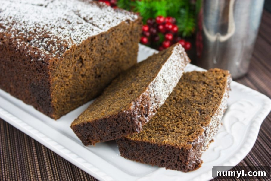 Spicy Gingerbread Loaf on a white plate with a couple of slices laying over, garnished with powdered sugar.
