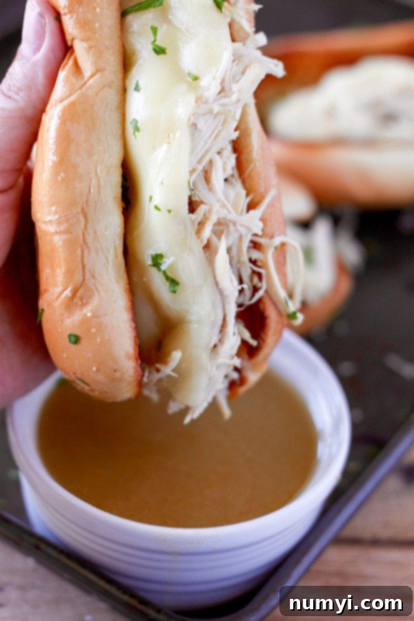 Tender Slow Cooker Chicken French Dip Sandwiches with melted provolone cheese and a side of au jus for dipping.