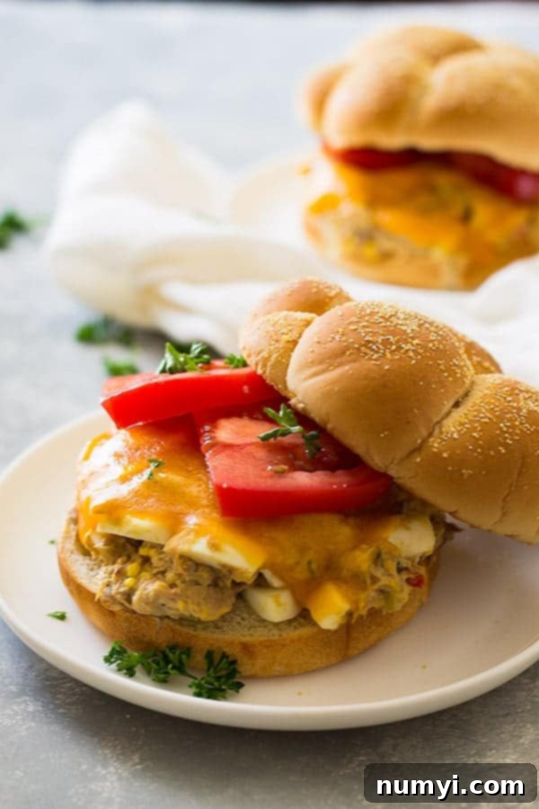 Golden Grilled Tuna Melts 2 Close up shot of sandwich with hamburger bun, sliced tomato, and cheese on white plate.