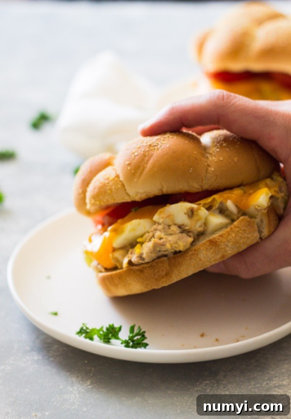 Golden Grilled Tuna Melts 3 Hand lifting tuna melt sandwich on hamburger bun from white plate.
