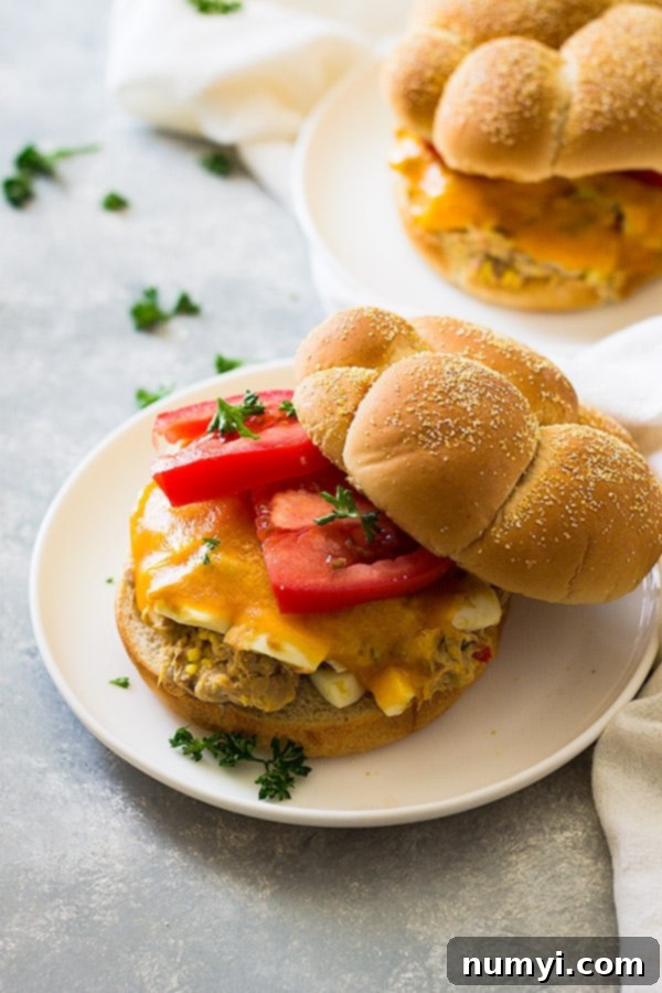 Golden Grilled Tuna Melts 4 Close up shot of tuna melt with hamburger bun, sliced tomato, and cheese on white plate.