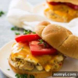 Golden Grilled Tuna Melts 5 Close up shot of sandwich with hamburger bun, sliced tomato, and cheese on white plate.