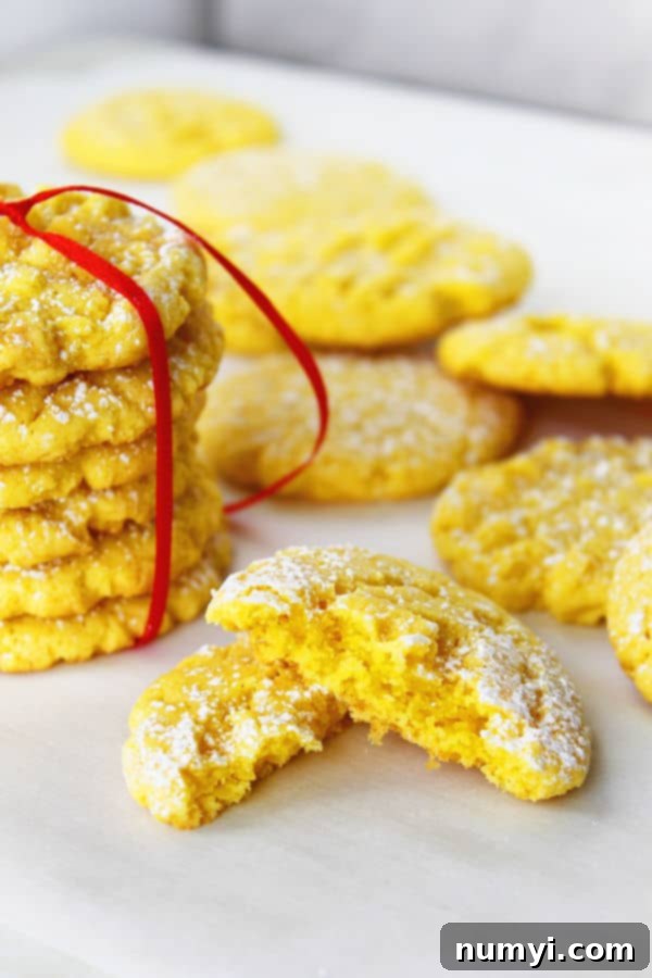 A pile of golden lemon cheesecake cookies, some tied with a bow, with one cut in half revealing its soft interior