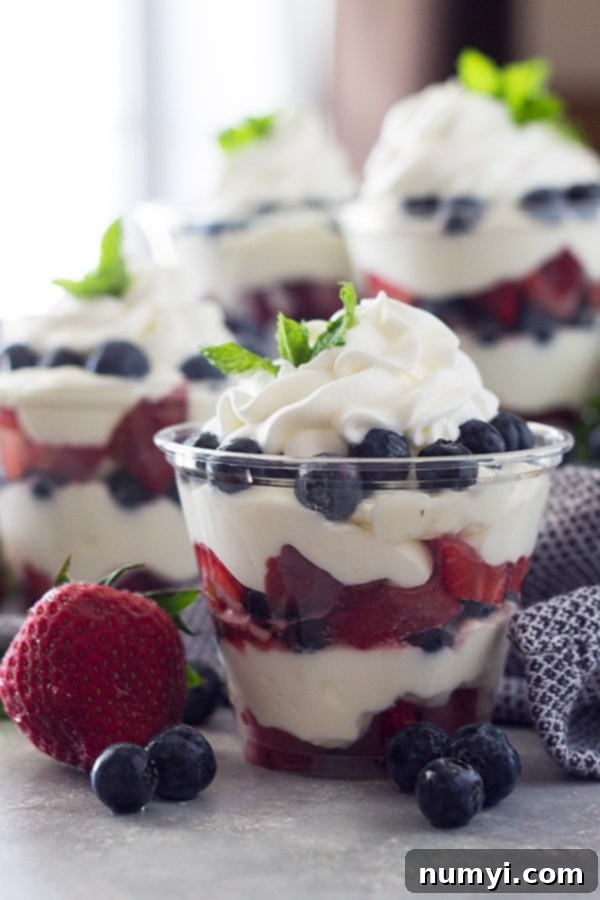 Eye-level view of two berry cheesecake cups with a blue linen towel, and more cups blurred in the background, showcasing the beautiful layers.
