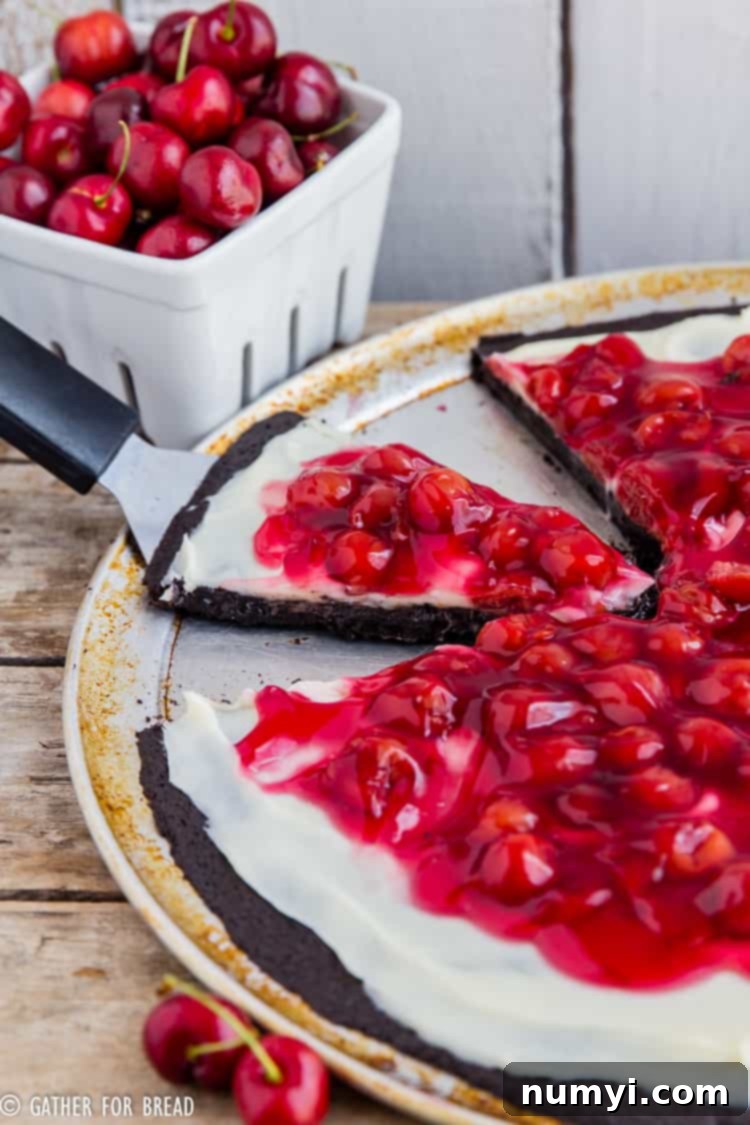 A slice of Chocolate Cherry Brownie Dessert Pizza, rich with chocolate and bright red cherries, on a serving board.