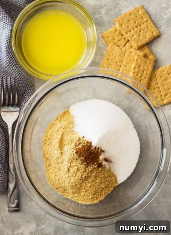 Perfect Homemade Graham Cracker Crust 5 overhead: graham cracker crumbs, sugar, and cinnamon in a glass mixing bowl with another glass bowl of melted butter to the side