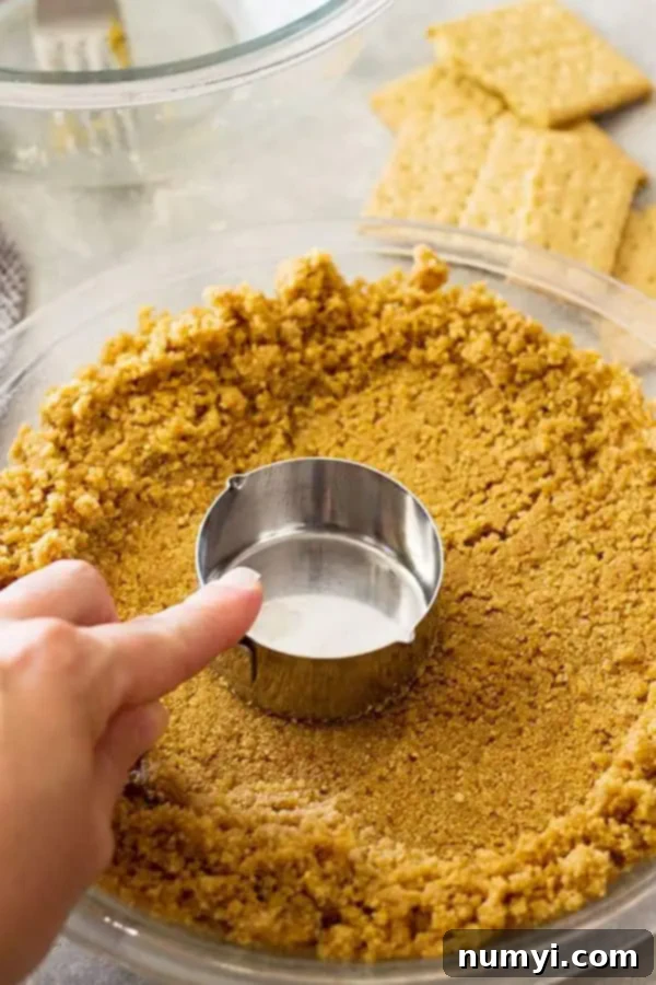 Perfect Homemade Graham Cracker Crust 8 a hand pressing homemade graham cracker pie crust into pie pan with measuring cup
