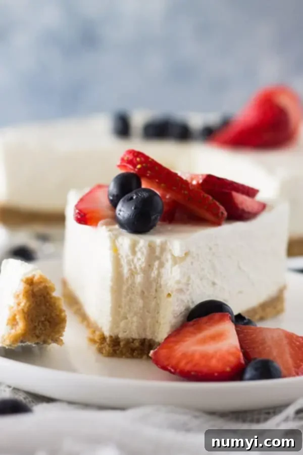 Creamy No-Bake Vanilla Cheesecake 6 Front view of a slice of no bake vanilla cheesecake with a forkful removed, topped with fresh berries.