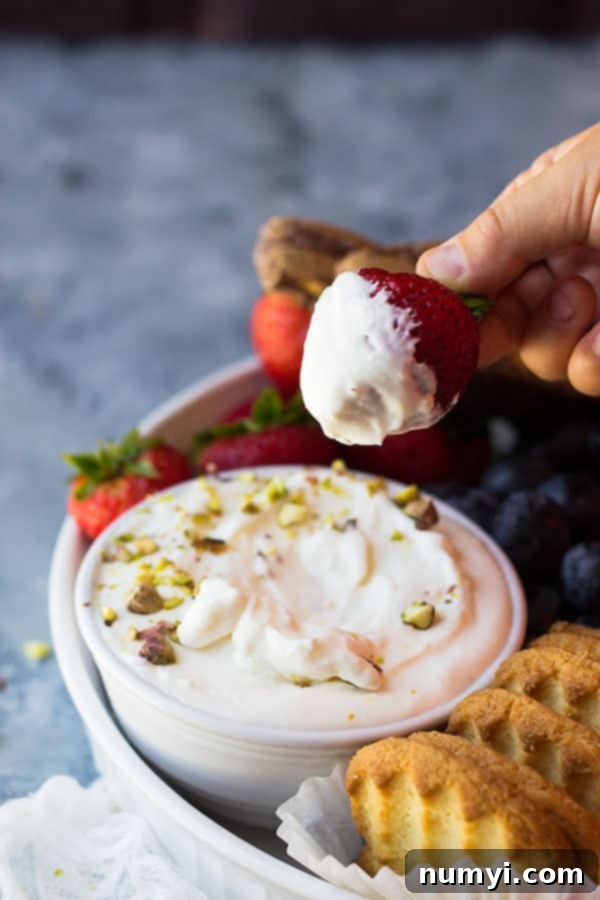 A vibrant fruit platter featuring a bowl of marshmallow fruit dip surrounded by strawberries, grapes, blueberries, and apple slices.