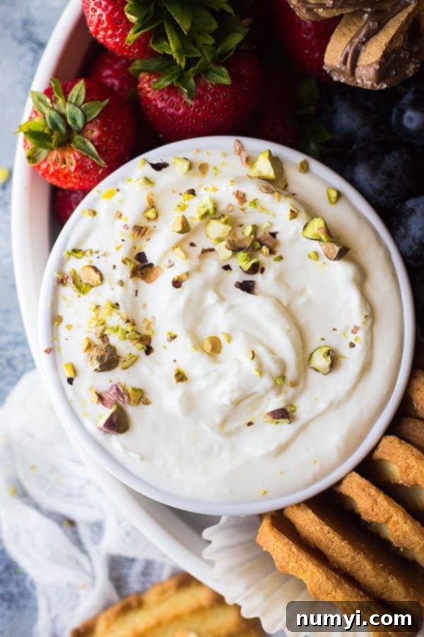 Marshmallow fruit dip in a bowl, glistening and creamy, with fresh berries scattered around it.