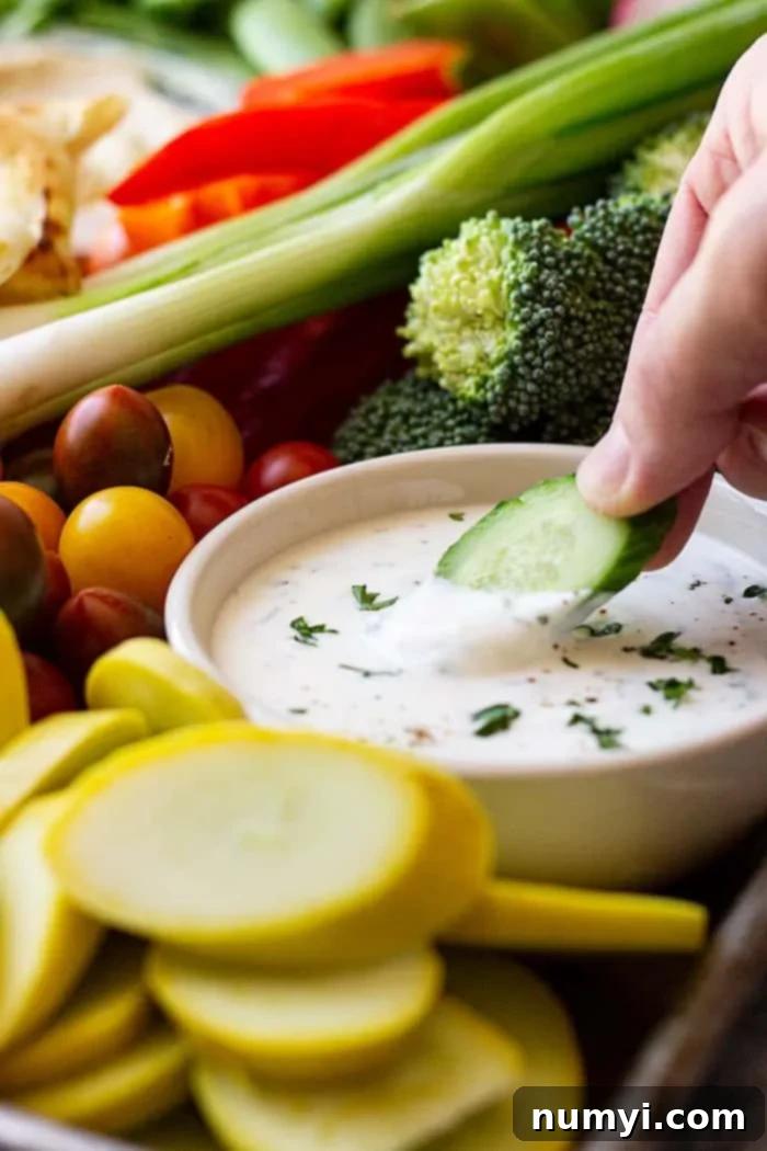 a hand with a cucumber dipping into a bowl of homemade ranch dressing on a veggie tray