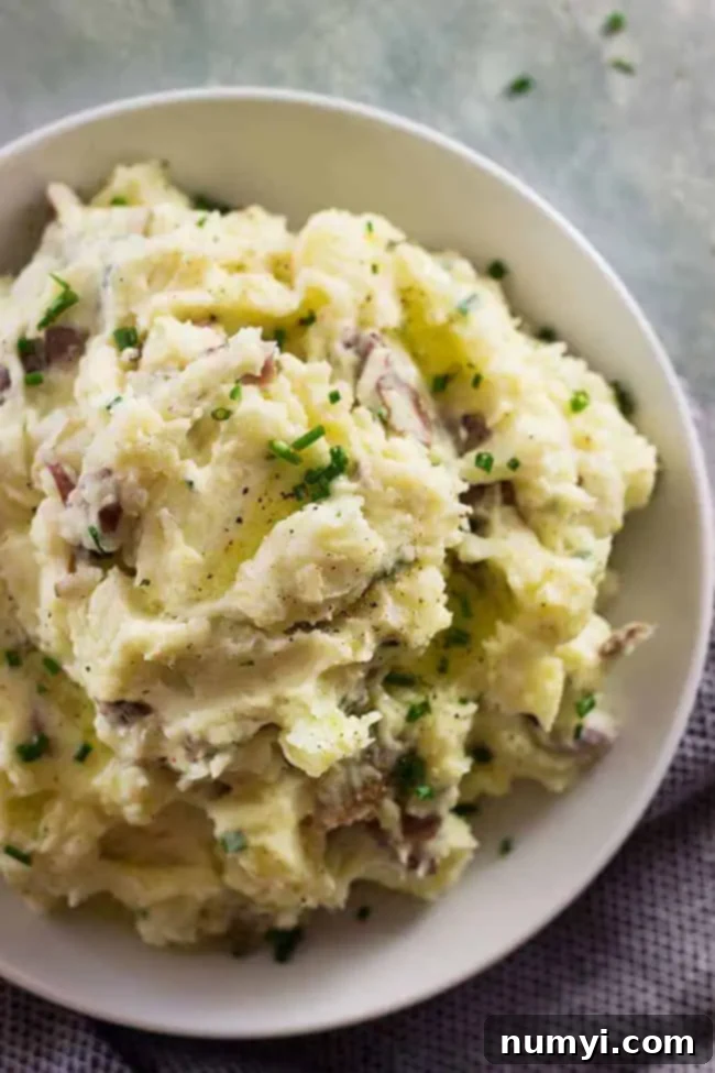 Overhead closeup of a heaping bowl of rustic mashed potatoes garnished with fresh chives, showcasing their comforting appeal.