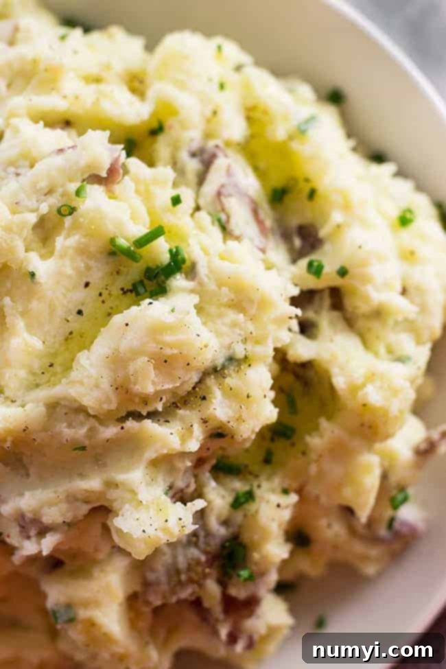 Overhead extreme closeup of a bowl of chunky mashed potatoes, seasoned perfectly and garnished with fresh green chives.