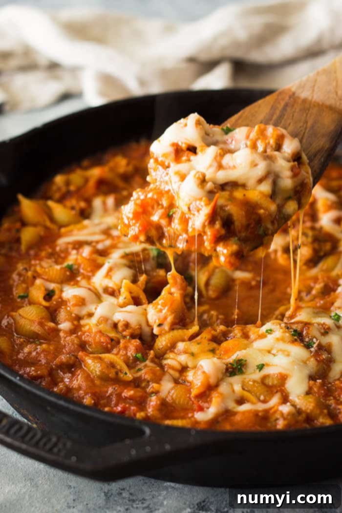 Wooden spoon serving One-Pot Italian Sausage Pasta from a skillet.